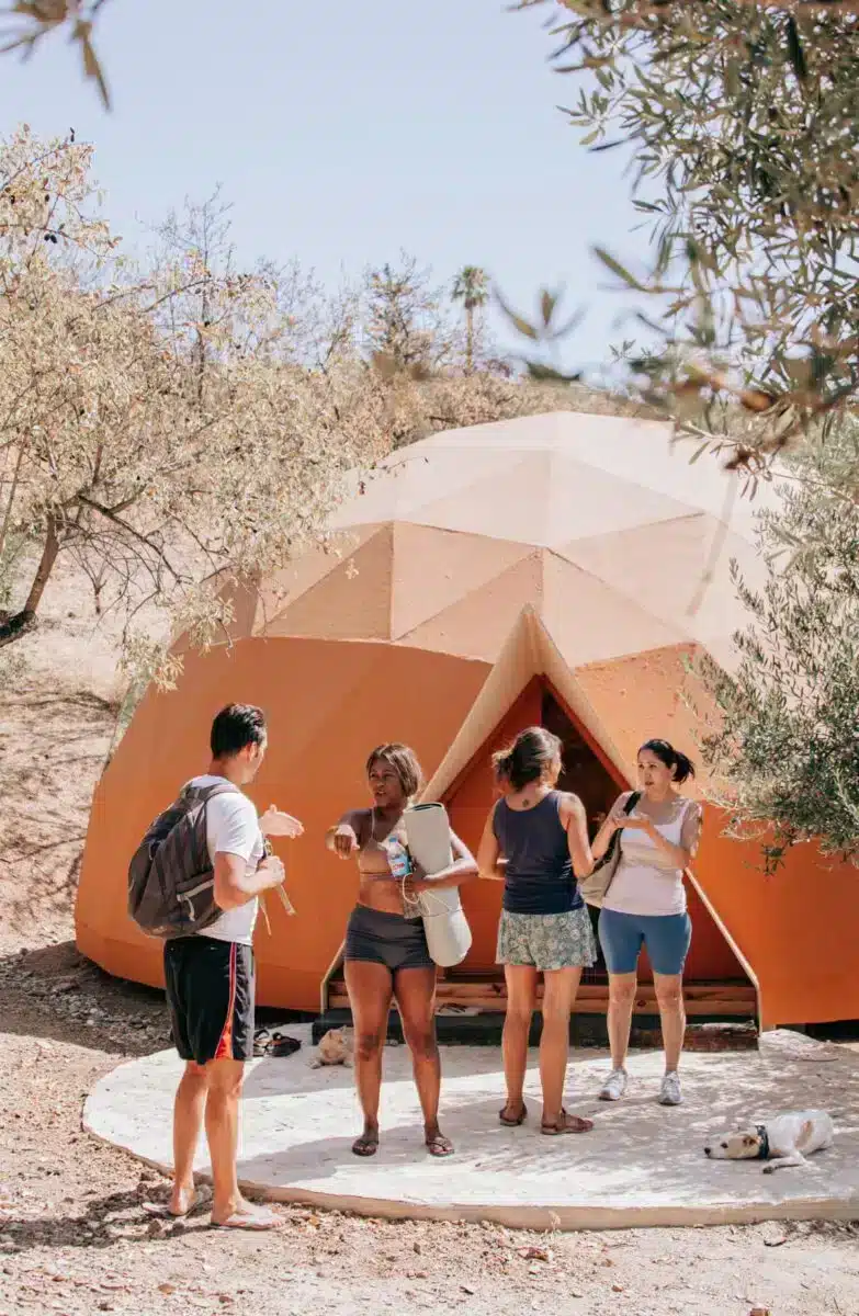 Group of guests chatting outside the geodesic dome and bell tent among olive trees at Costa del Soul retreat