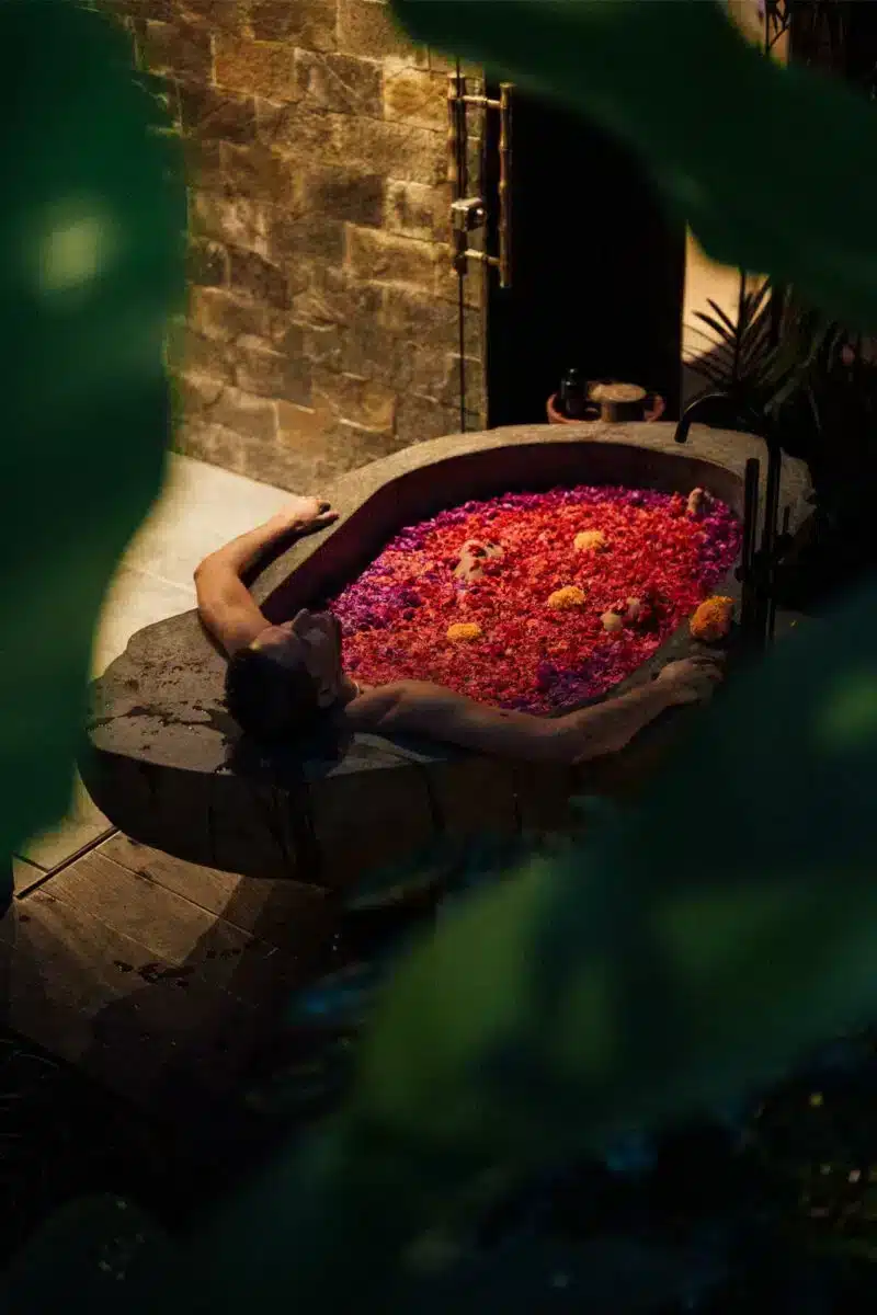 Close-up of Balinese flower bath with vibrant red and pink petals in stone bathtub at Desa Hay Bali