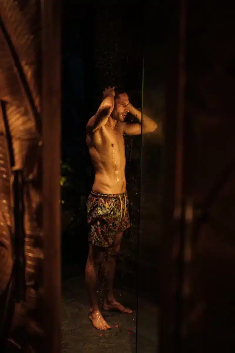 Guest taking an outdoor shower surrounded by tropical plants and natural stone walls at Desa Hay Bali