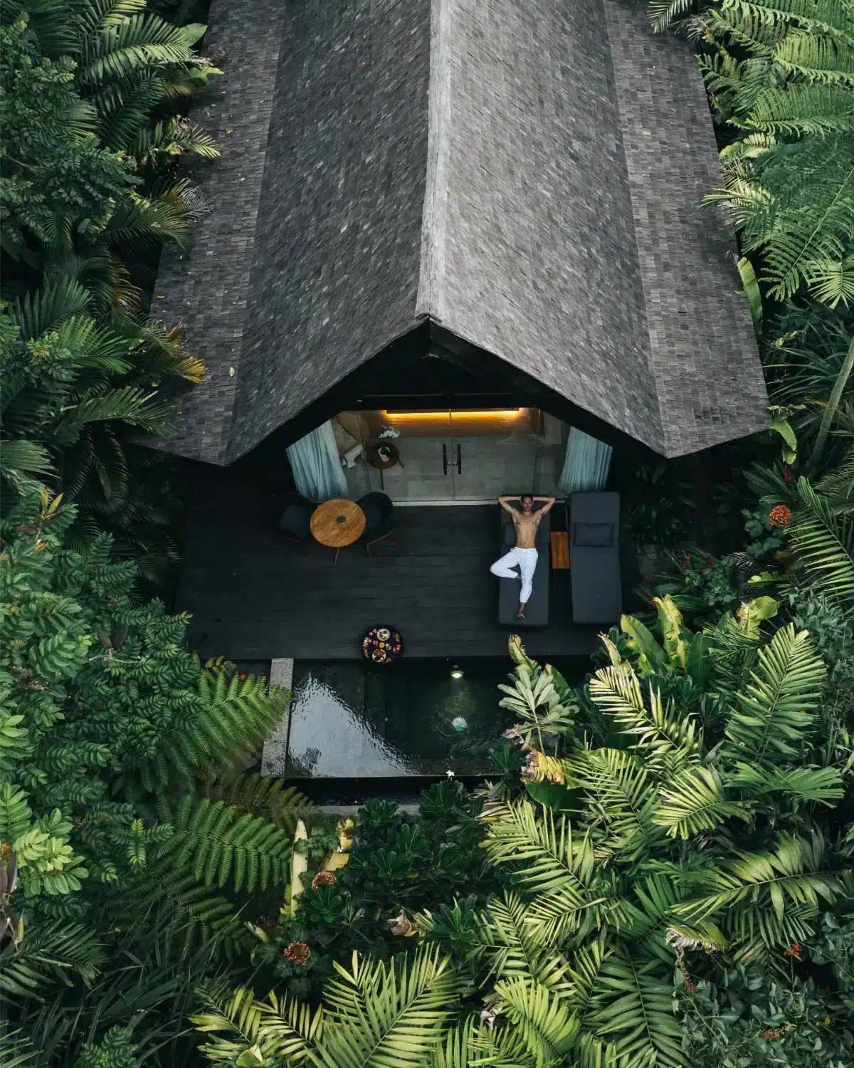 Aerial drone view of Premium Jabu Villa at Desa Hay Bali showing guest relaxing on wooden deck terrace with plunge pool surrounded by lush tropical garden