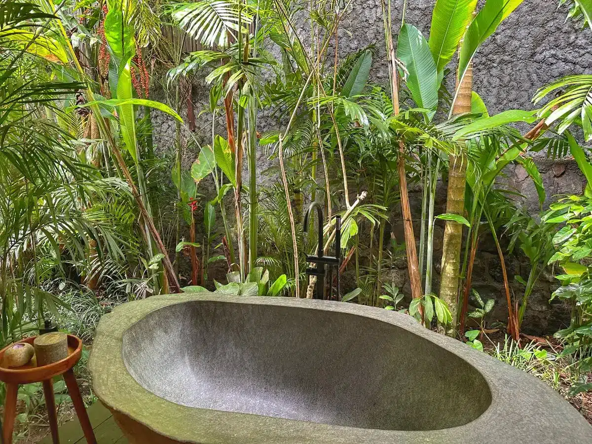 Outdoor stone bathtub nestled in lush tropical garden with natural stone walls at Desa Hay Bali