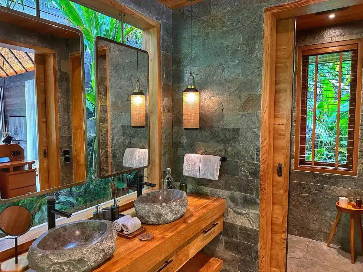 Spacious bathroom with natural stone vanity basin wooden countertop and large mirror at Desa Hay Bali villa