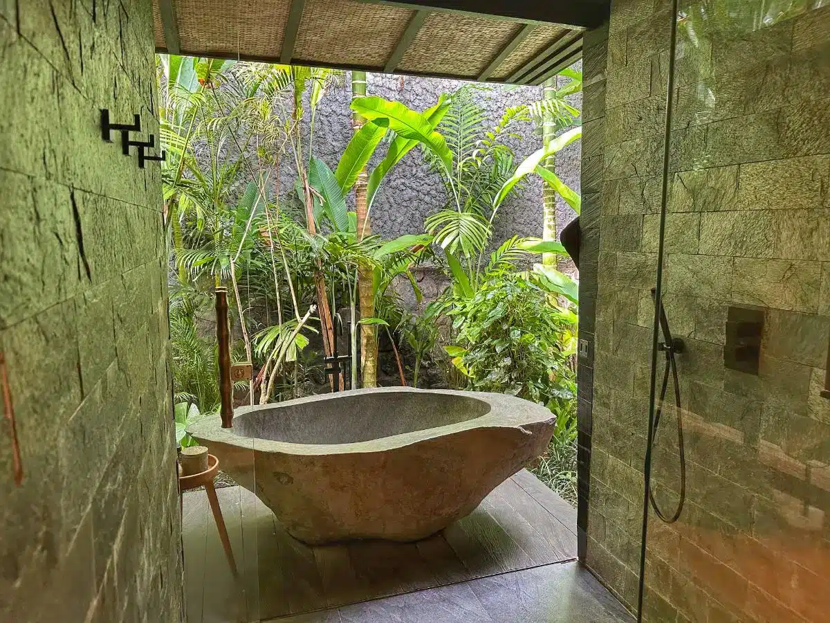 Open-air outdoor stone bathtub surrounded by tropical plants with garden shower at Desa Hay Bali