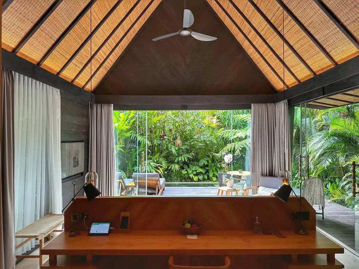 Desa Hay Bali villa interior with wooden desk and ceiling fan looking out through floor-to-ceiling windows to tropical garden terrace