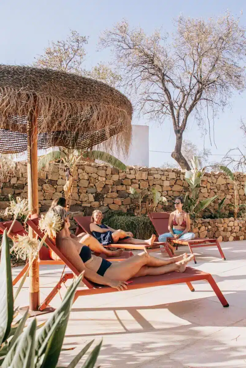 Guests relaxing on deck chairs by the pool under thatched shade with stone walls at Costa del Soul retreat Málaga
