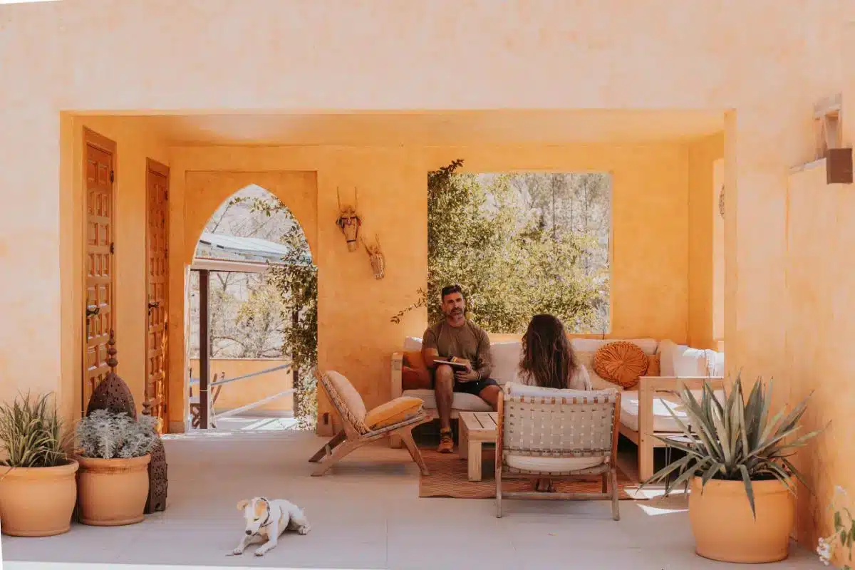 Two guests chatting in a terracotta-colored covered terrace with arched doorways and mountain views at Costa del Soul