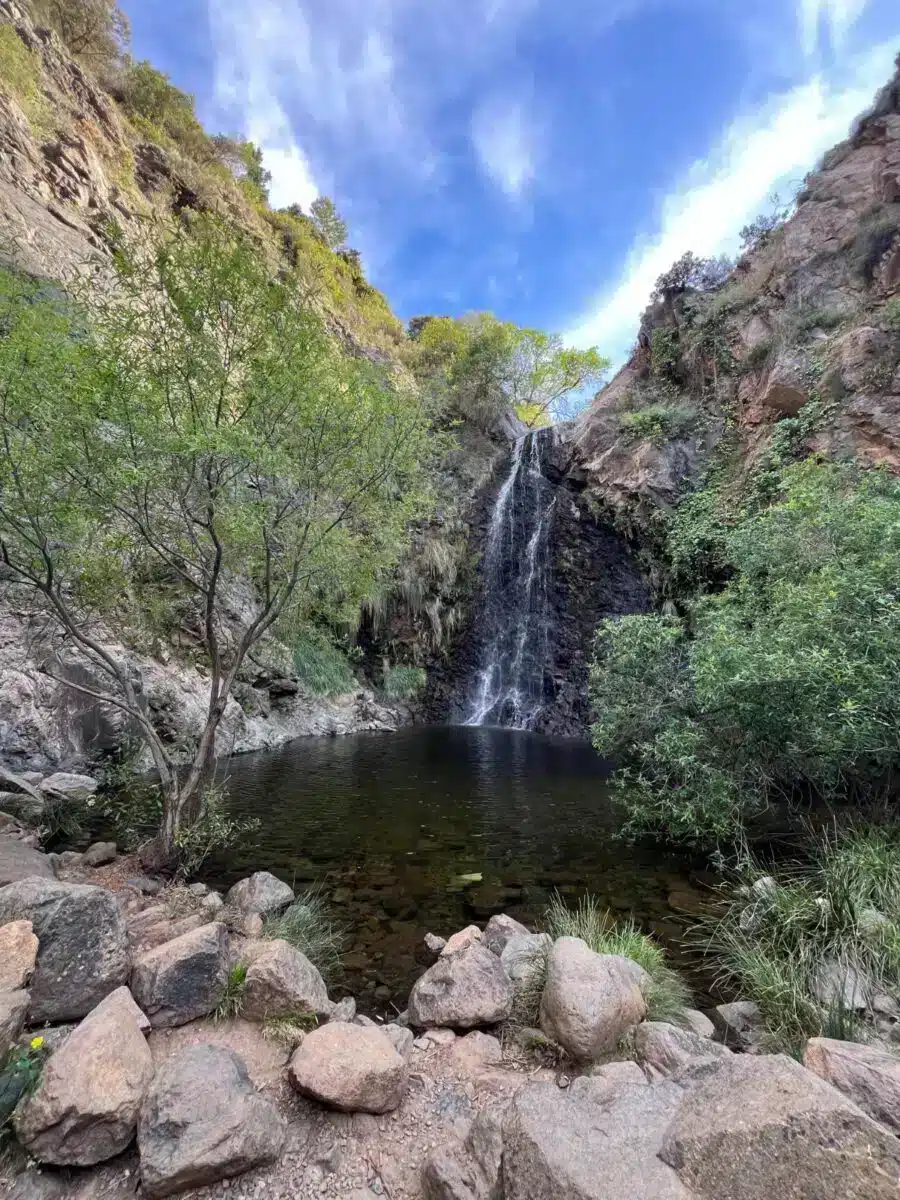 Waterfall cascading into a natural rock pool surrounded by lush vegetation and blue sky near Costa del Soul Málaga