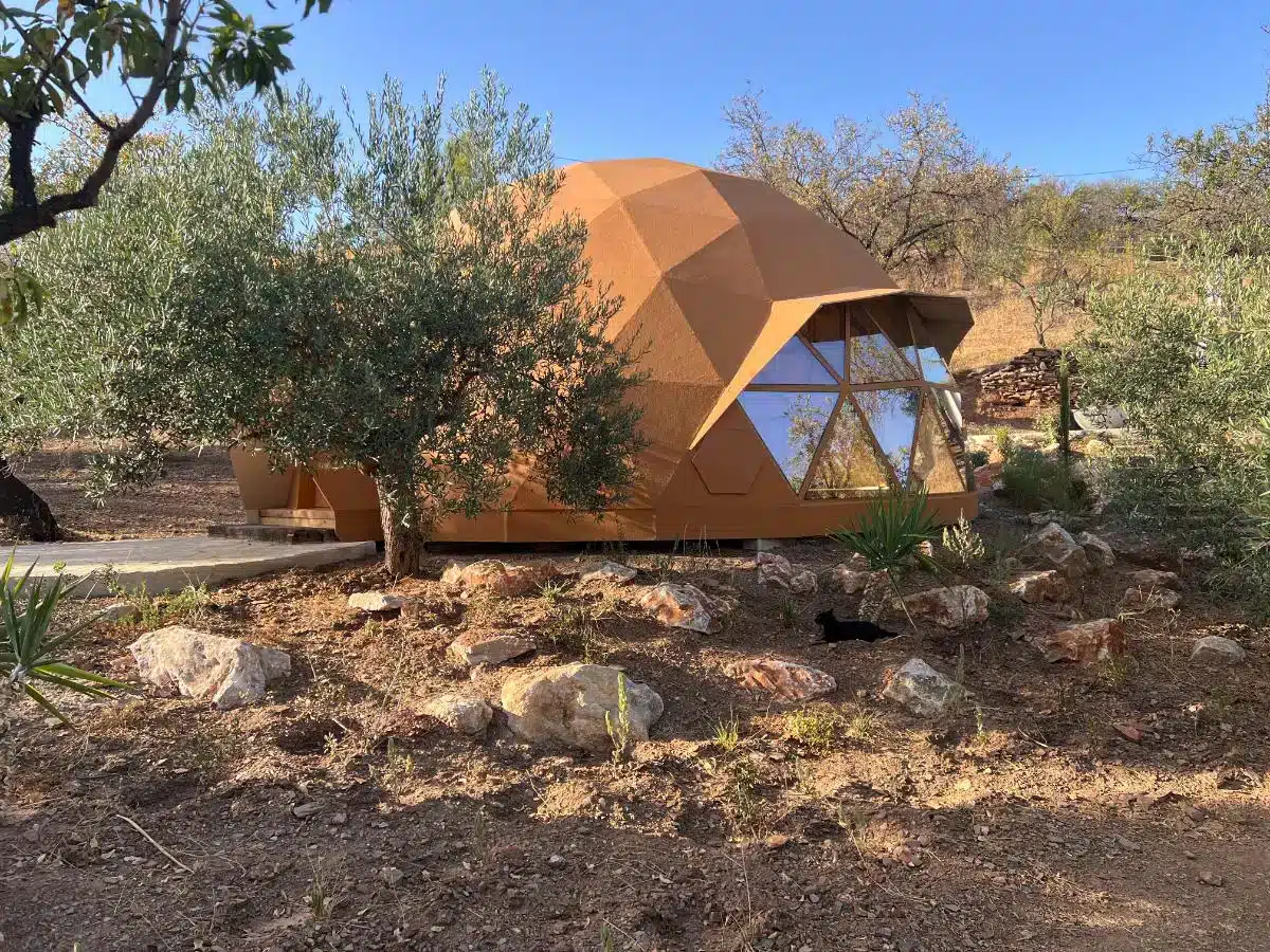 Geodesic dome among olive trees and rocky Mediterranean terrain with blue sky and mountains at Costa del Soul Guaro