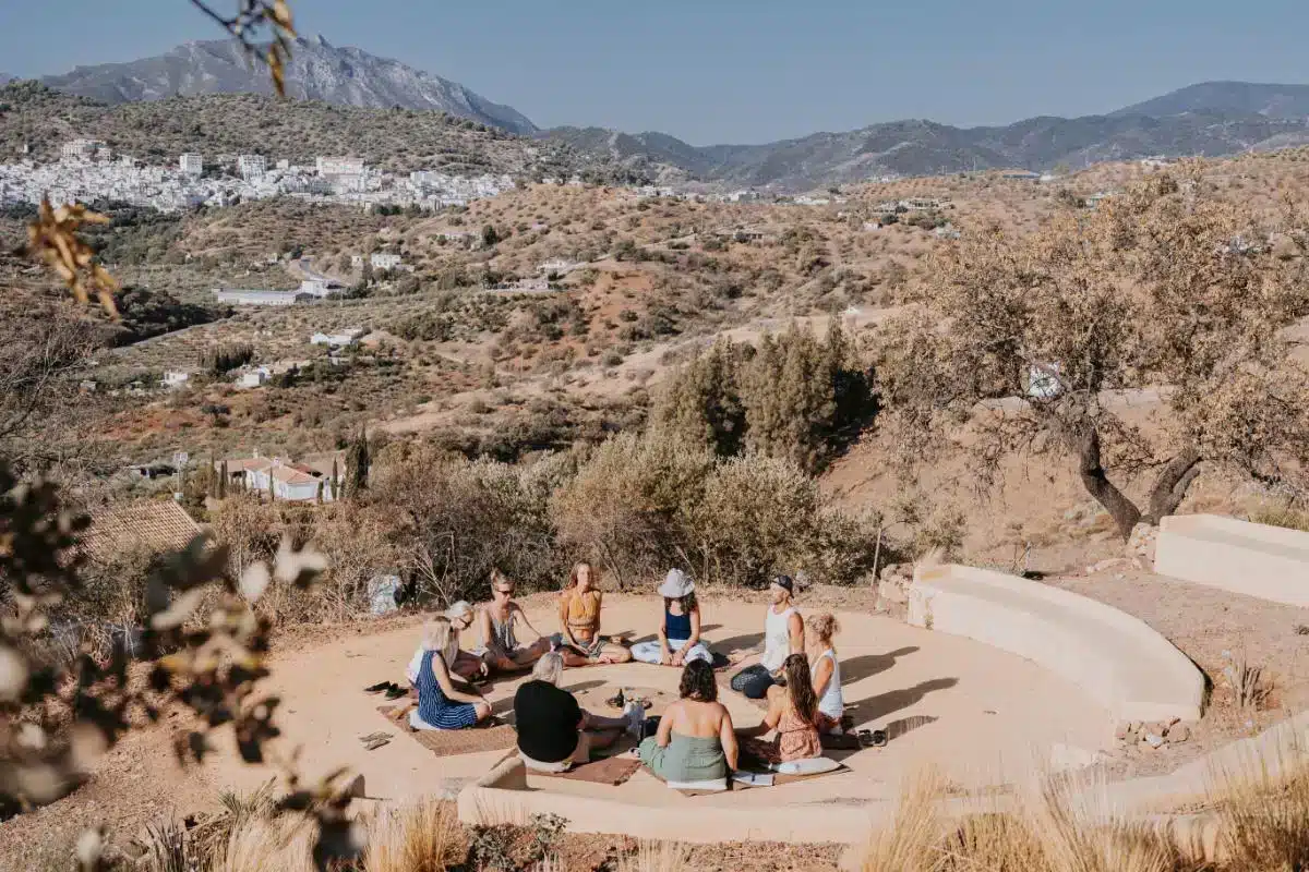 Group of guests sitting in a circle for outdoor meditation on rocky terrain with mountain village views at Costa del Soul Málaga