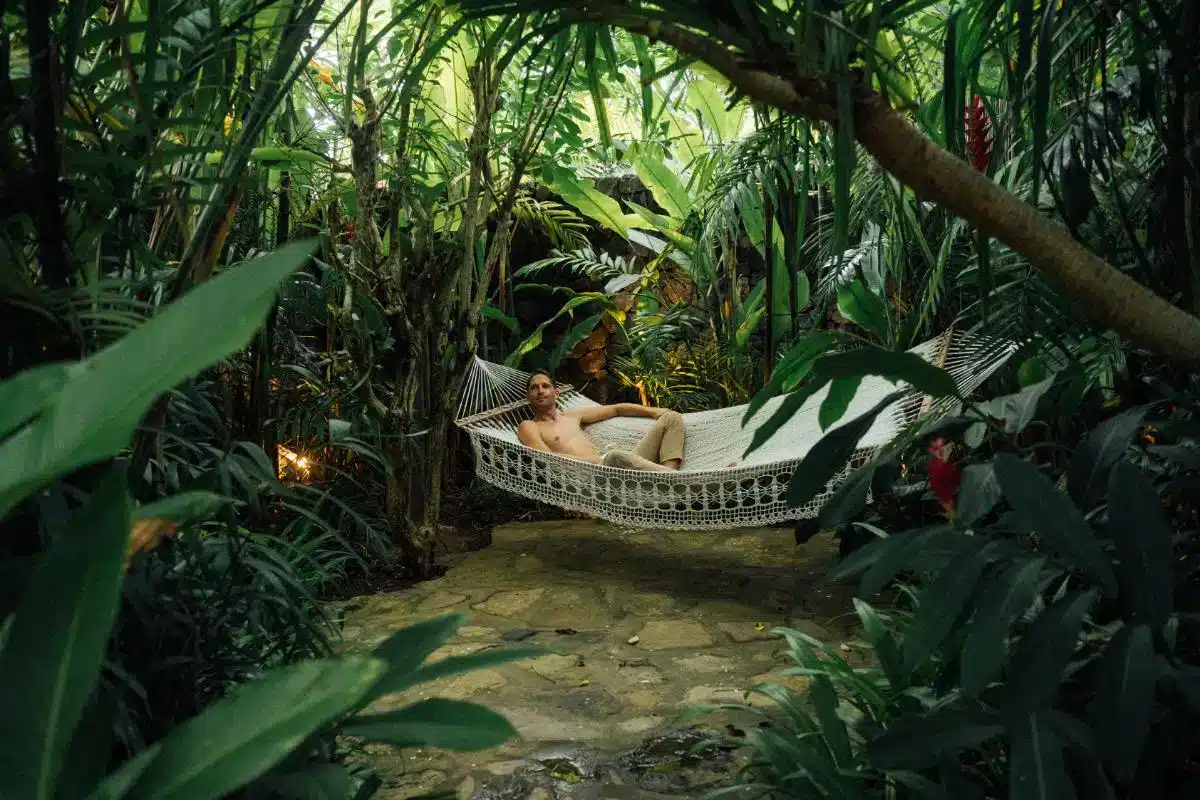 Guest relaxing in outdoor bathtub viewed through tropical foliage at Desa Hay Bali