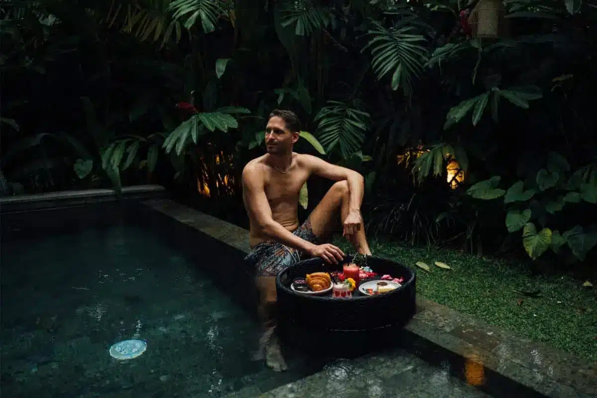 Guest sitting by the private plunge pool with a floating breakfast tray among tropical plants at Desa Hay Bali
