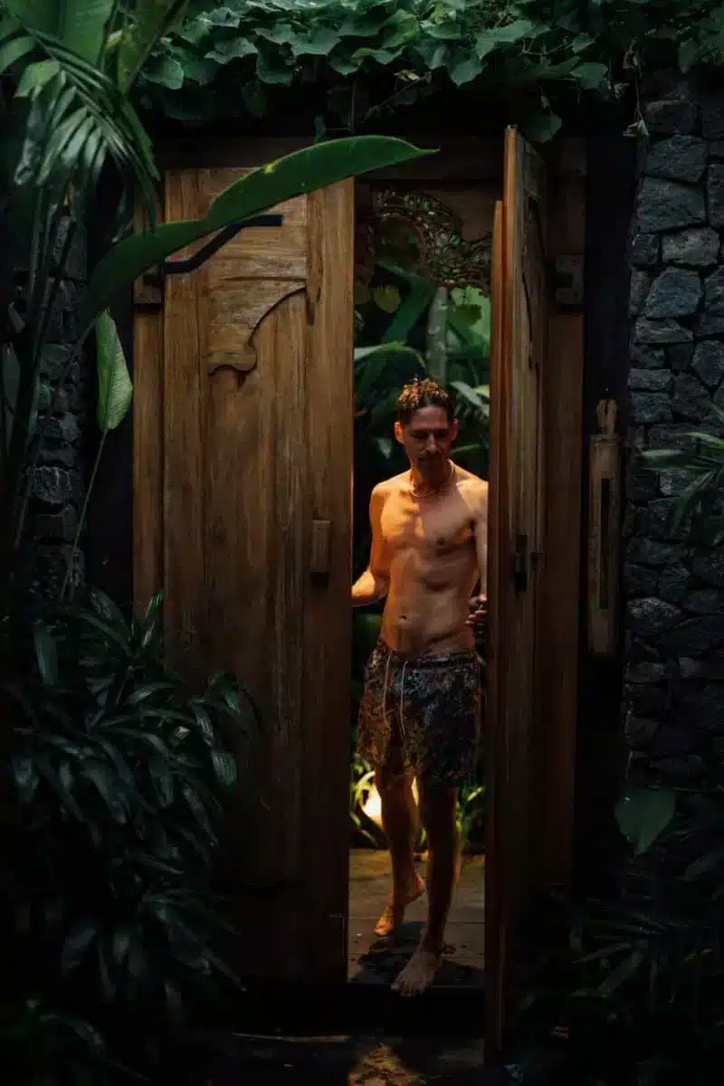 Guest standing in the wooden doorway of the villa surrounded by stone walls and tropical plants at Desa Hay Bali