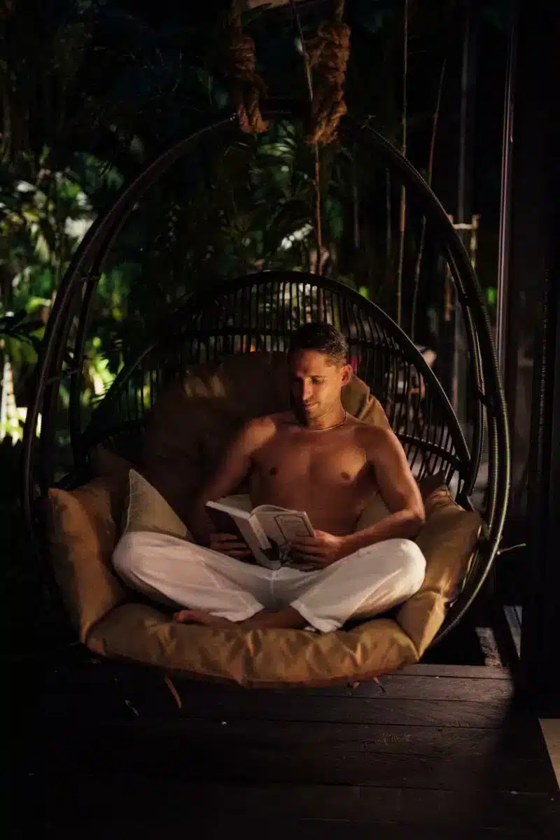 Guest reading a book in hanging egg chair on the villa terrace surrounded by tropical plants at Desa Hay Bali