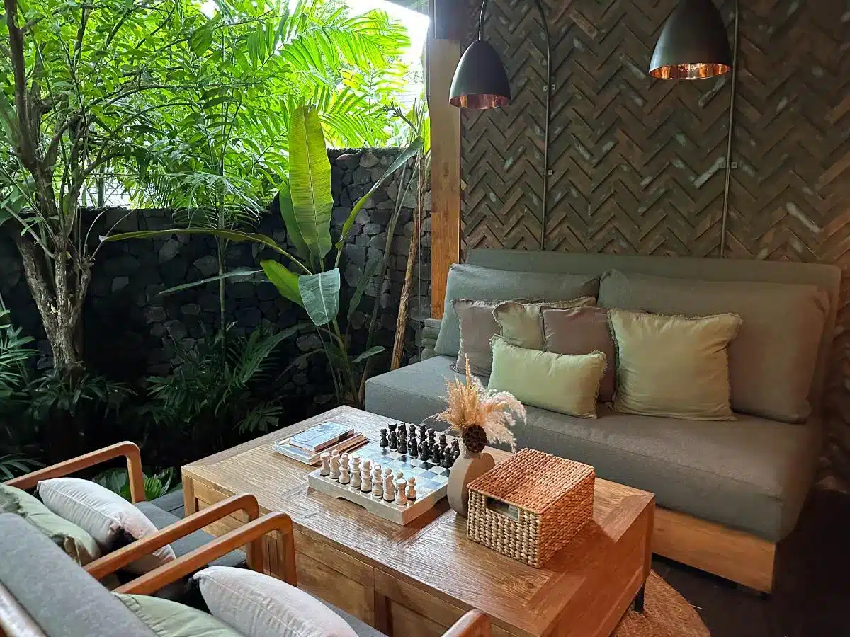 Outdoor lounge area at Ijo by Desa Hay with cushioned sofa drinks and board games surrounded by tropical plants