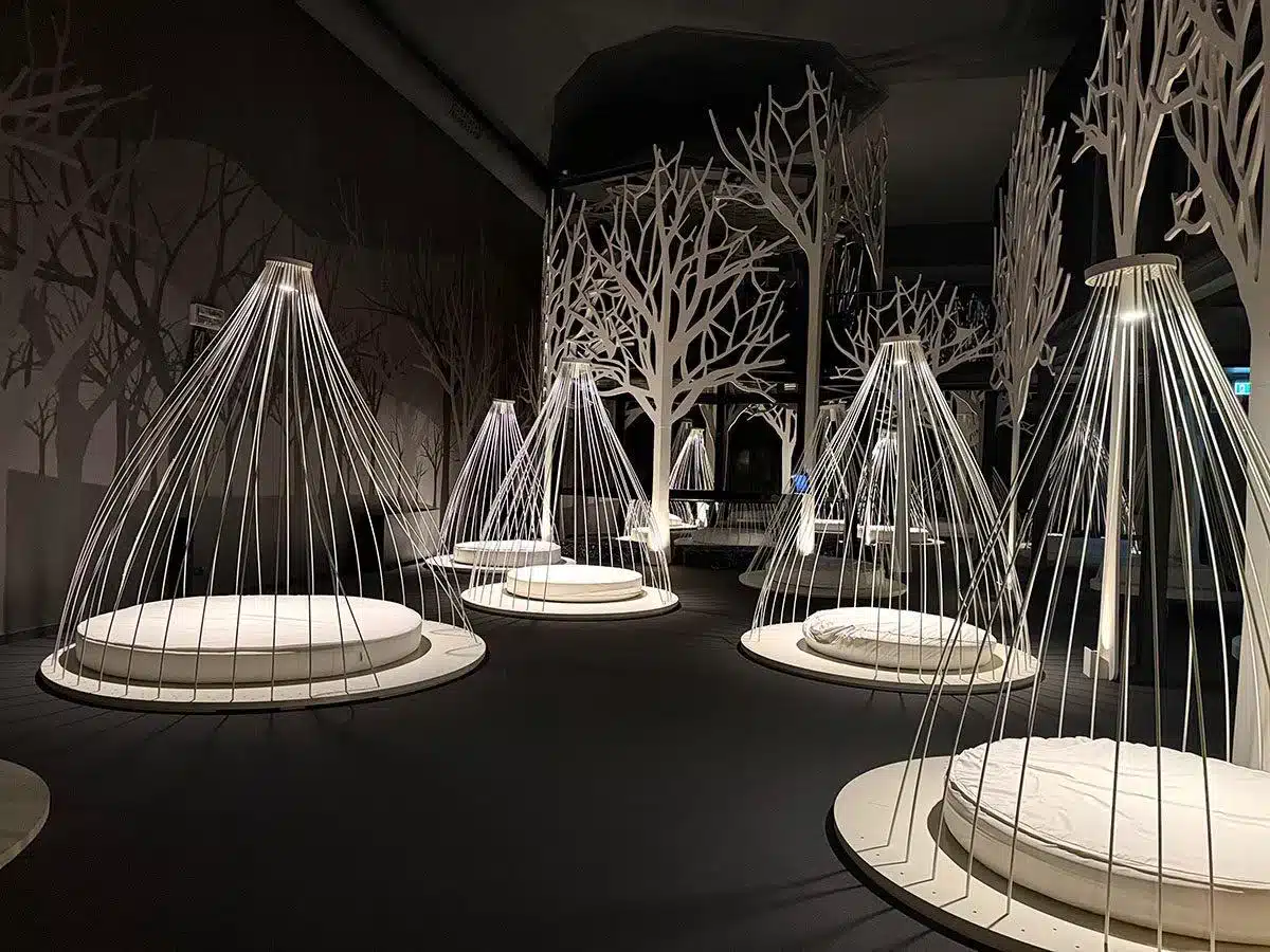 Künstlerische weiße Drahtbaum- und käfigartige Lichtinstallationen in einem dunklen immersiven Raum im QC Terme Milano
