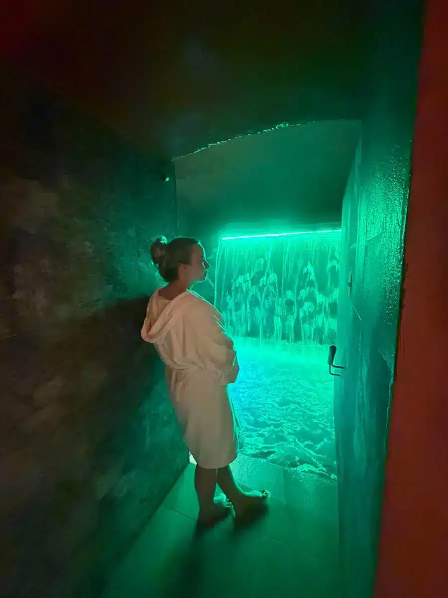 Gast im Bademantel in einem grün beleuchteten Salzraum mit strukturierten Wänden im QC Terme Milano