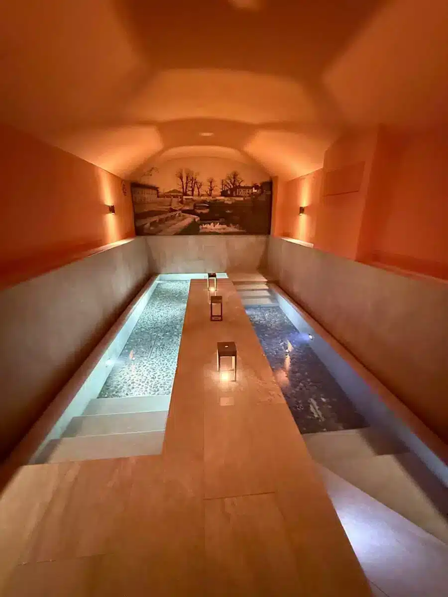 Warm bernsteinfarben beleuchteter Thermalbecken-Korridor mit Kerzen und Wandkunst im QC Terme Milano