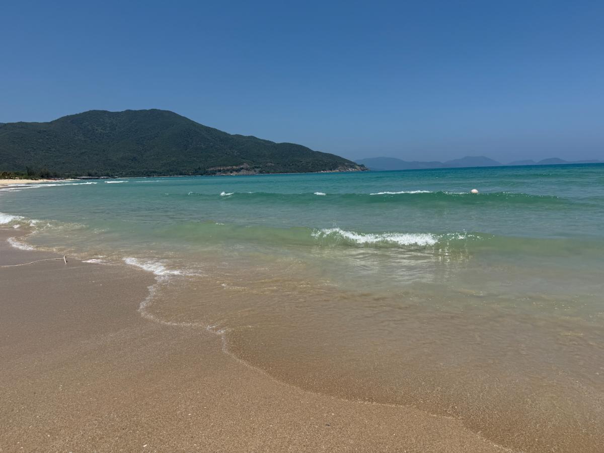 Cam Ranh Strand mit türkisfarbenem Wasser, weißem Sand und grünen Bergen im Hintergrund bei The Anam
