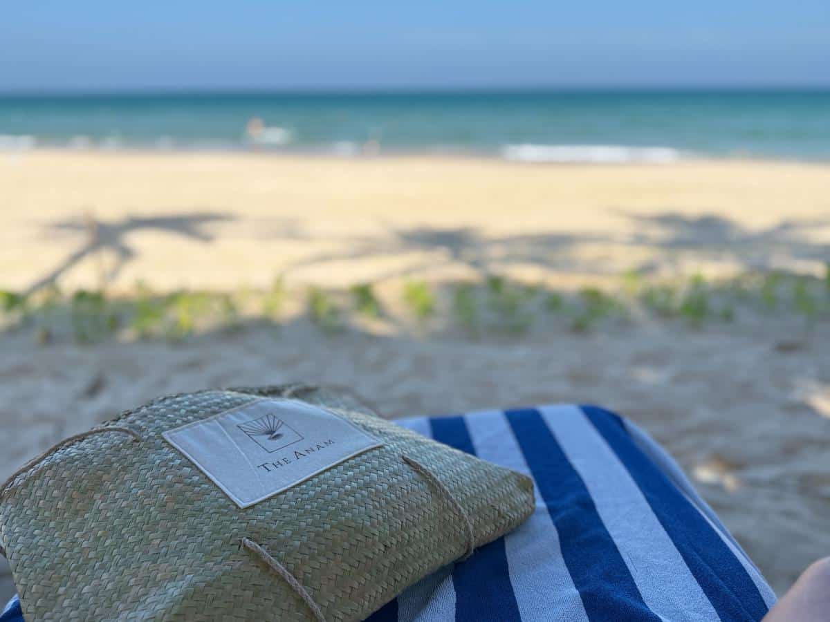 Gestreiftes Strandtuch und Sonnenhut auf dem weißen Sand unter dem Schatten der Palmen im The Anam Cam Ranh