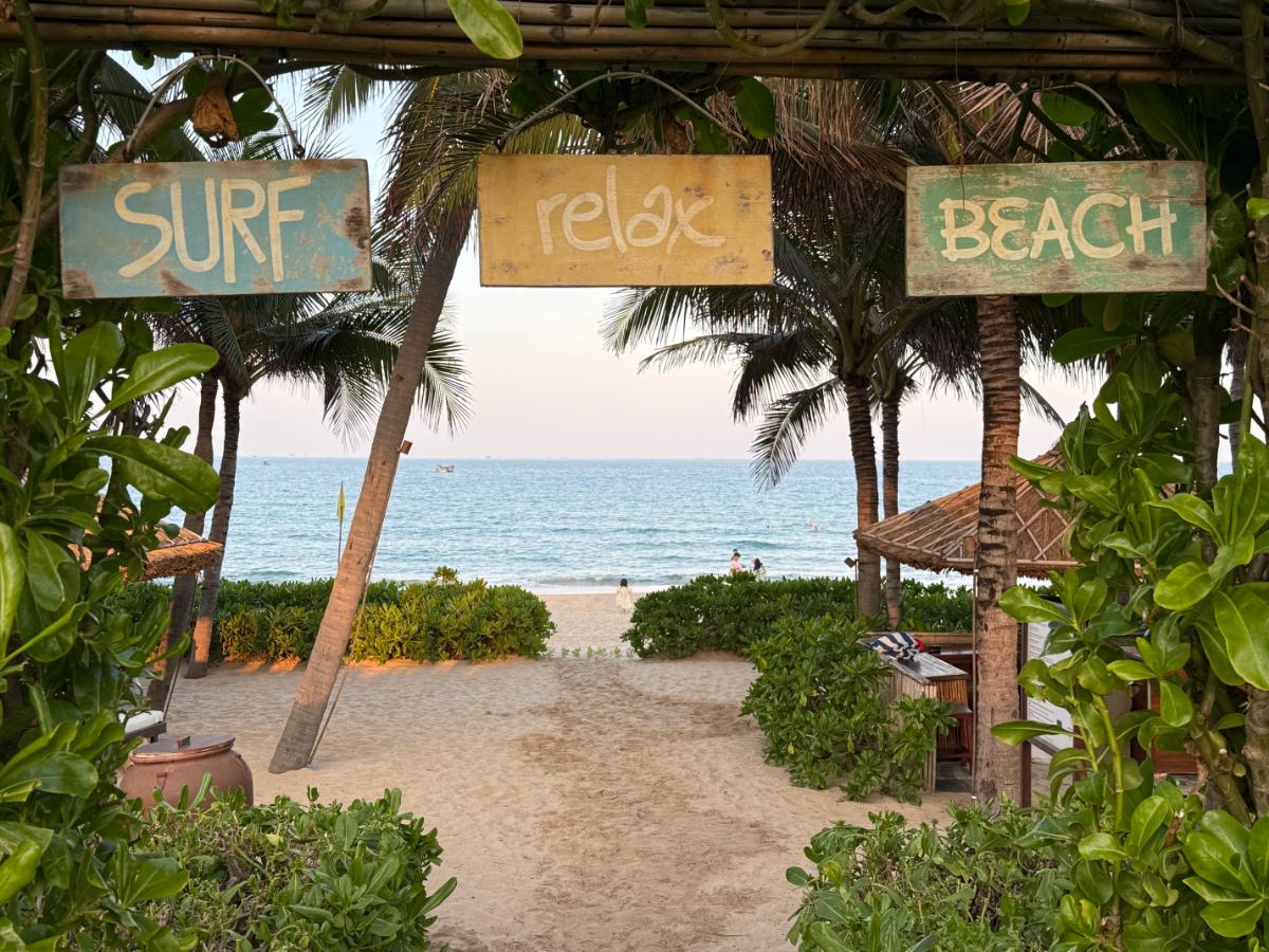 Strandeingang mit hölzernen Surf Relax und Beach Schildern unter Palmen im The Anam Cam Ranh