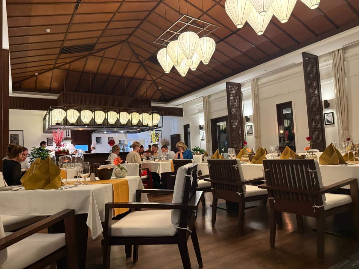 Das Interieur des Restaurants im Kolonialstil mit Hängelampen, weißen Tischdecken und Gästen beim Essen im The Anam Cam Ranh