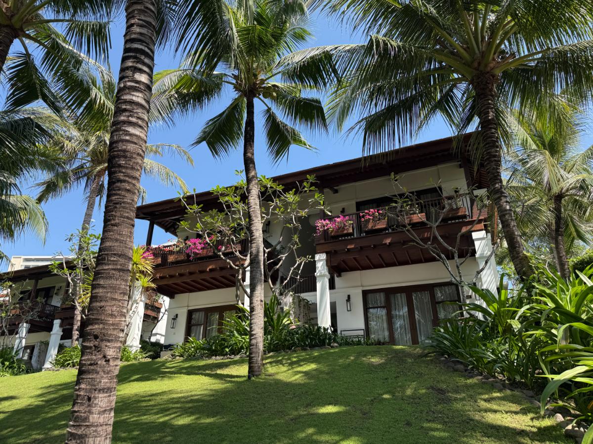 Resortgebäude im Kolonialstil mit Holzbalkonen, Bougainvillea-Blumen und Palmen im The Anam Cam Ranh