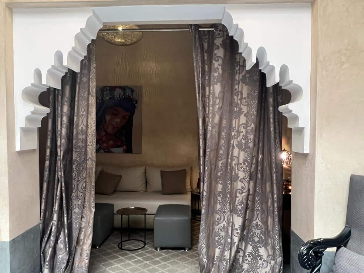 Marokkanischer Sitzbereich mit drapierten Vorhängen Bogendurchgang gepolstertem Sofa und gerahmter Kunst im Les Bains D’Orient Hammam in Marrakesch