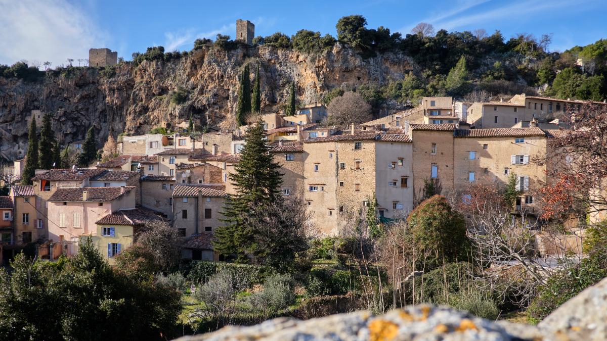 Panoramic view of Cotignac village nestled into the hillside with stone houses and the dramatic cliff face in Provence