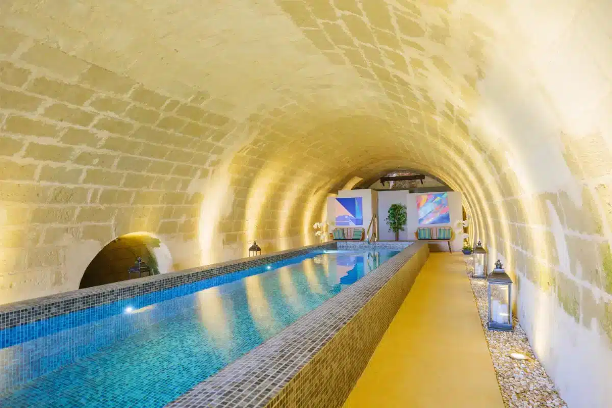Unterirdischer Troglodyten-Spa-Pool im Château de Candes im Loire-Tal, der durch einen uralten gewölbten Steintunnel verläuft, mit blau leuchtendem Wasser