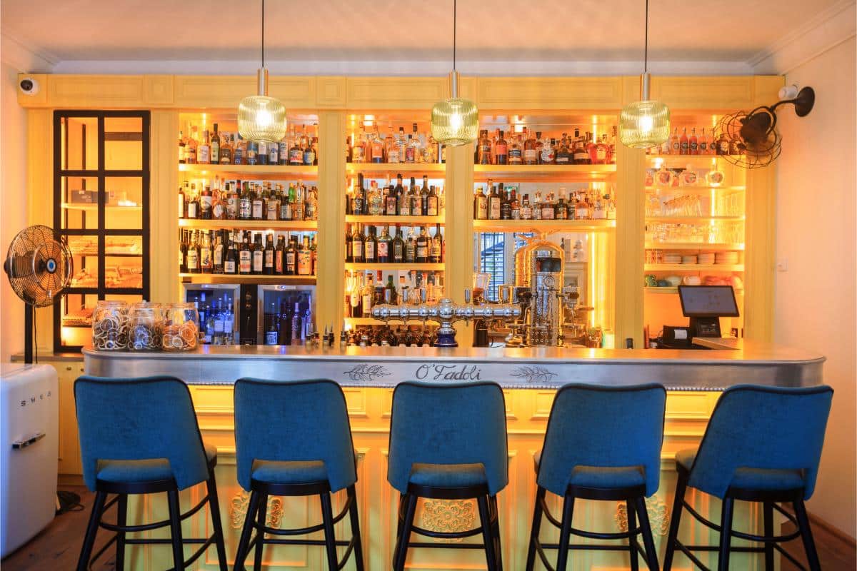 Pastis bar at Lou Calen with illuminated shelves of bottles blue velvet bar stools and warm ambient lighting
