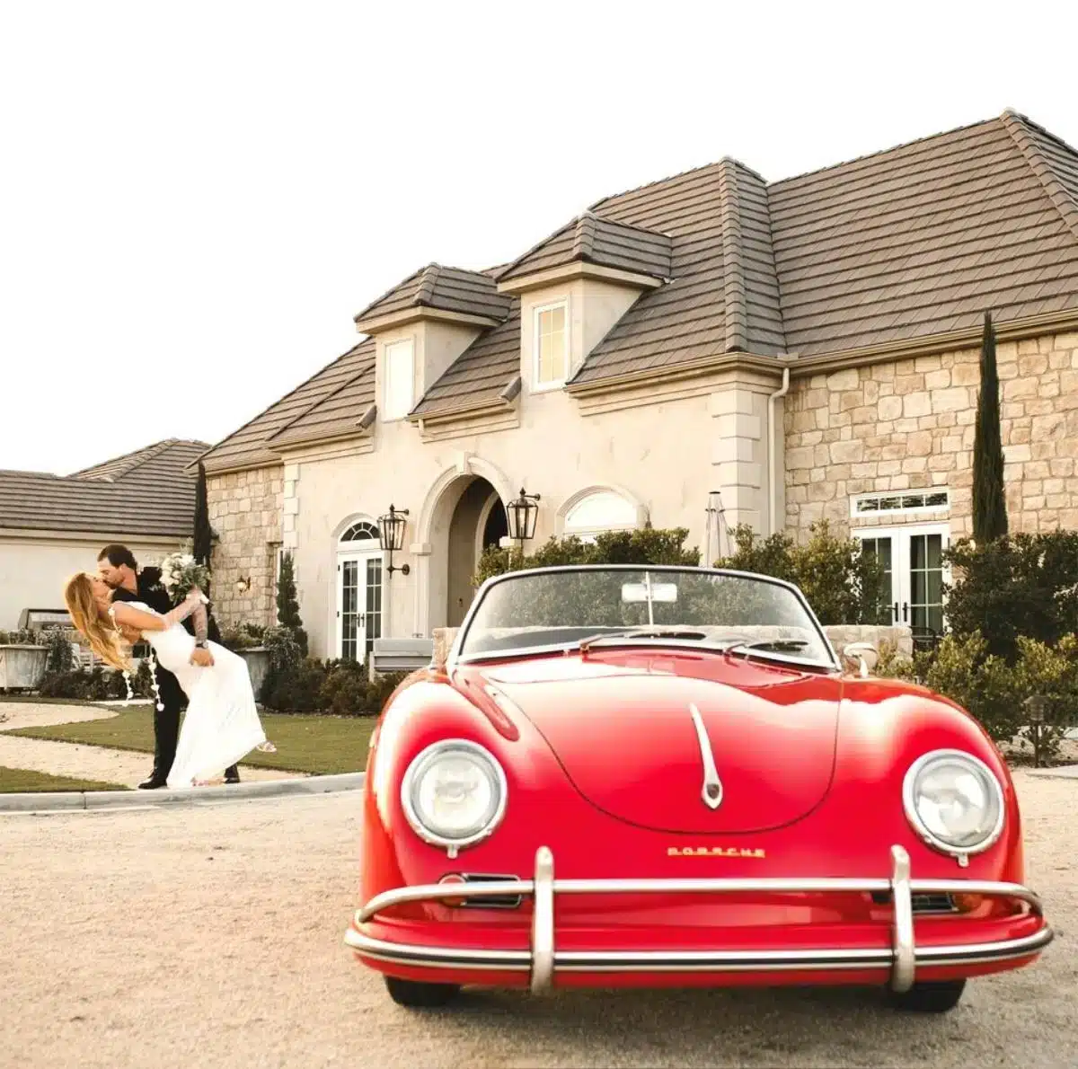 A bride and groom sharing a romantic dip kiss in front of a classic red Porsche 356 convertible parked in front of the Domaine Chardonnay estate