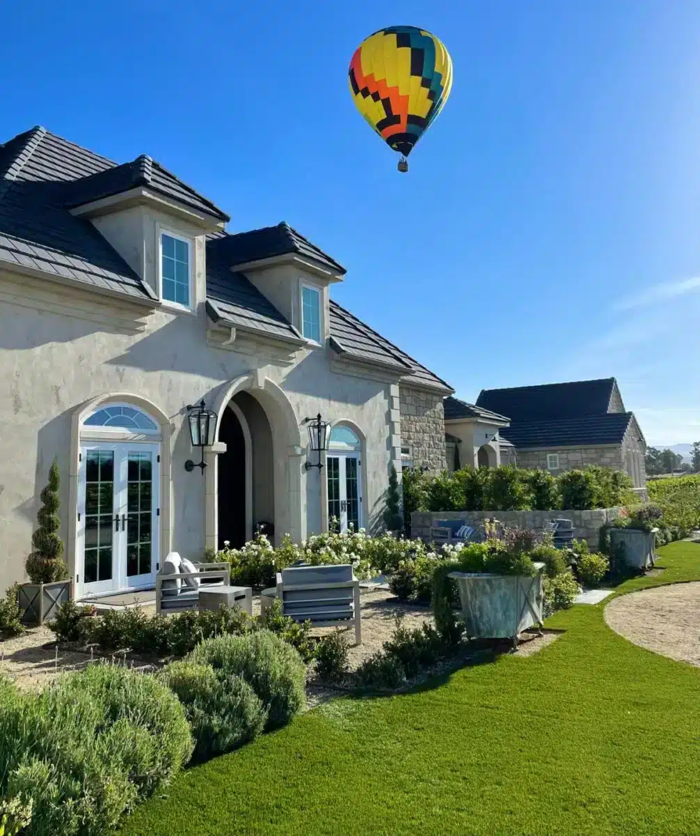 Domaine Chardonnay French-inspired estate exterior in Temecula wine country with a colourful hot air balloon above the manicured garden and guest terrace