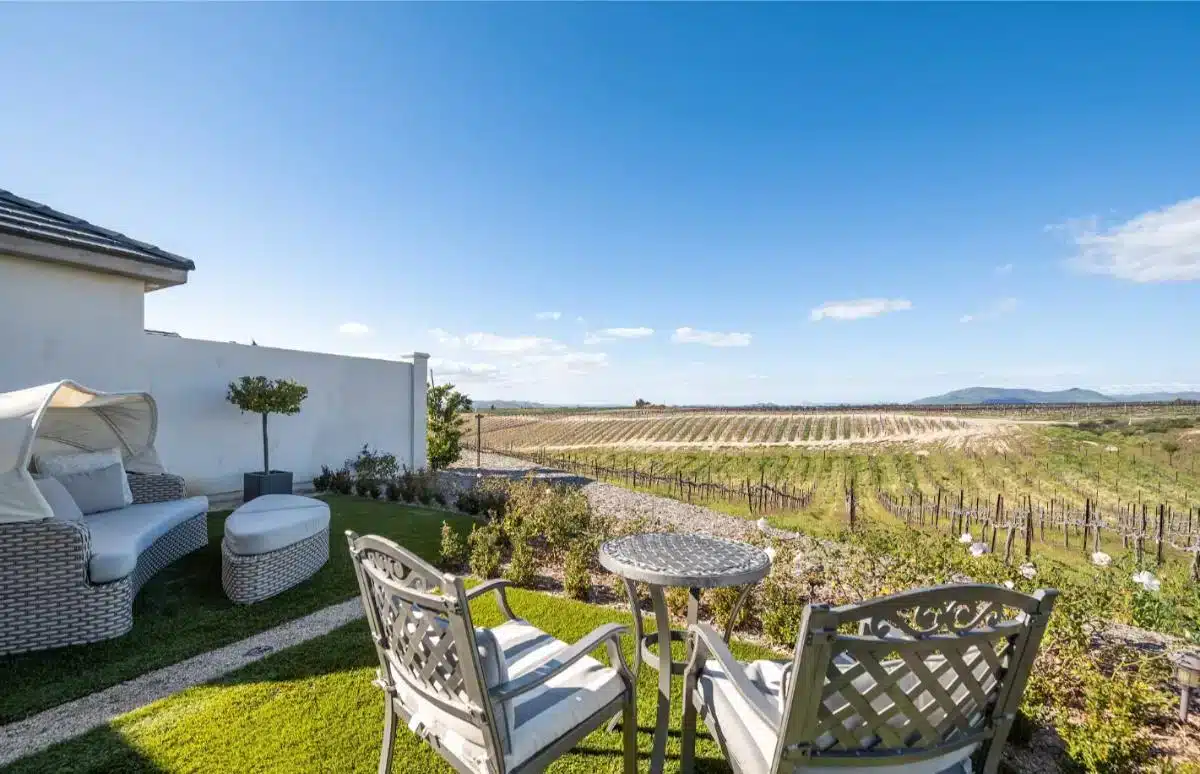 Private outdoor terrace of a Domaine Chardonnay guest suite with wicker patio furniture overlooking the vineyard rows and Temecula valley mountains beyond