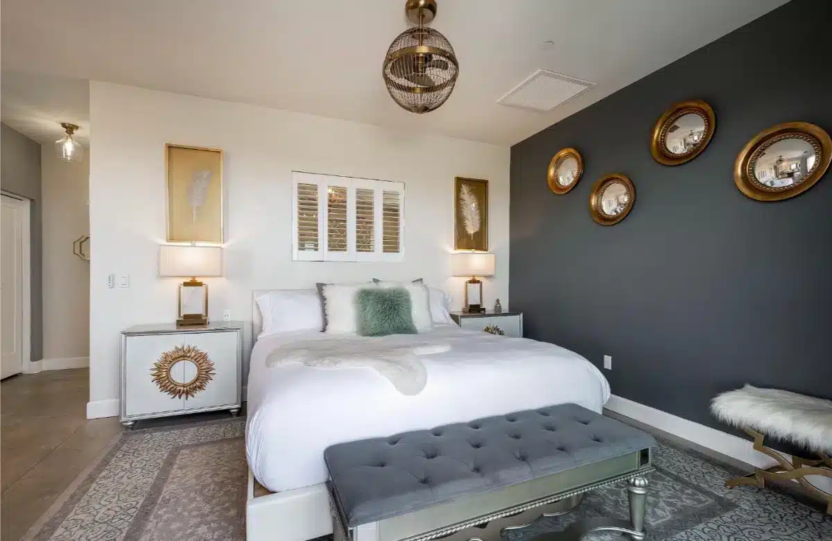 Elegantly designed guest suite at Domaine Chardonnay with dark charcoal accent wall, sunburst mirror, rattan pendant light and crisp white bed linen