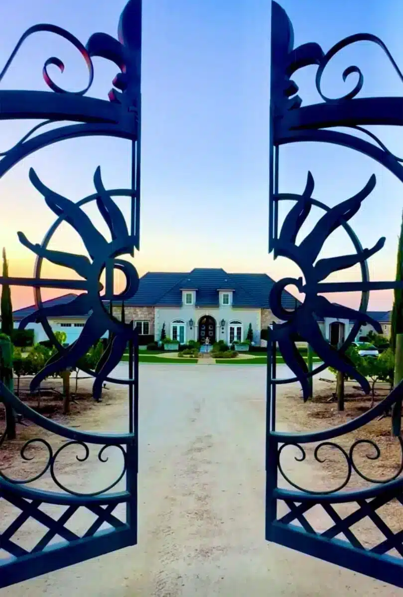 Ornate wrought-iron front gate of Domaine Chardonnay opening to reveal the main estate building and manicured grounds at dusk