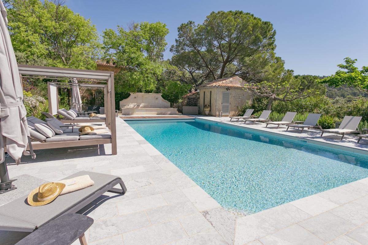 Swimming pool with stone terrace and sunbeds surrounded by lush greenery at Lou Calen Cotignac