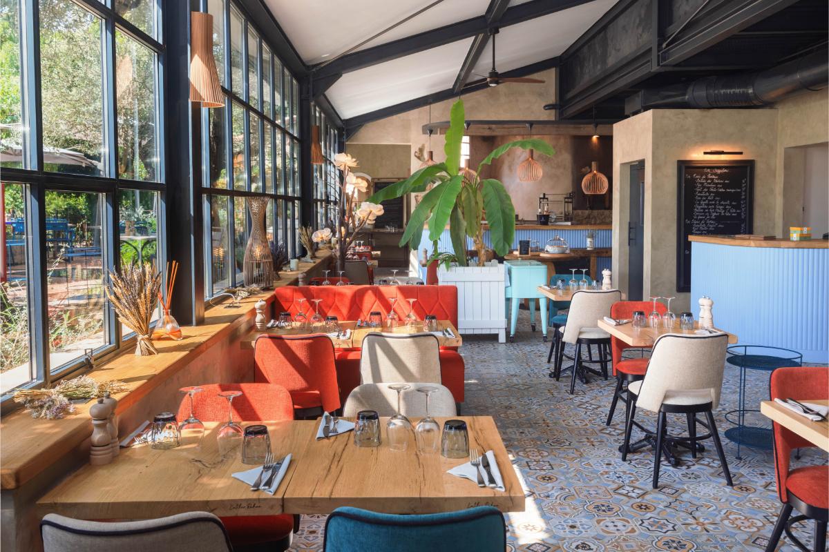 Le Bistrot glass-ceiling conservatory dining room with red banquettes wooden tables and terrazzo floor at Lou Calen