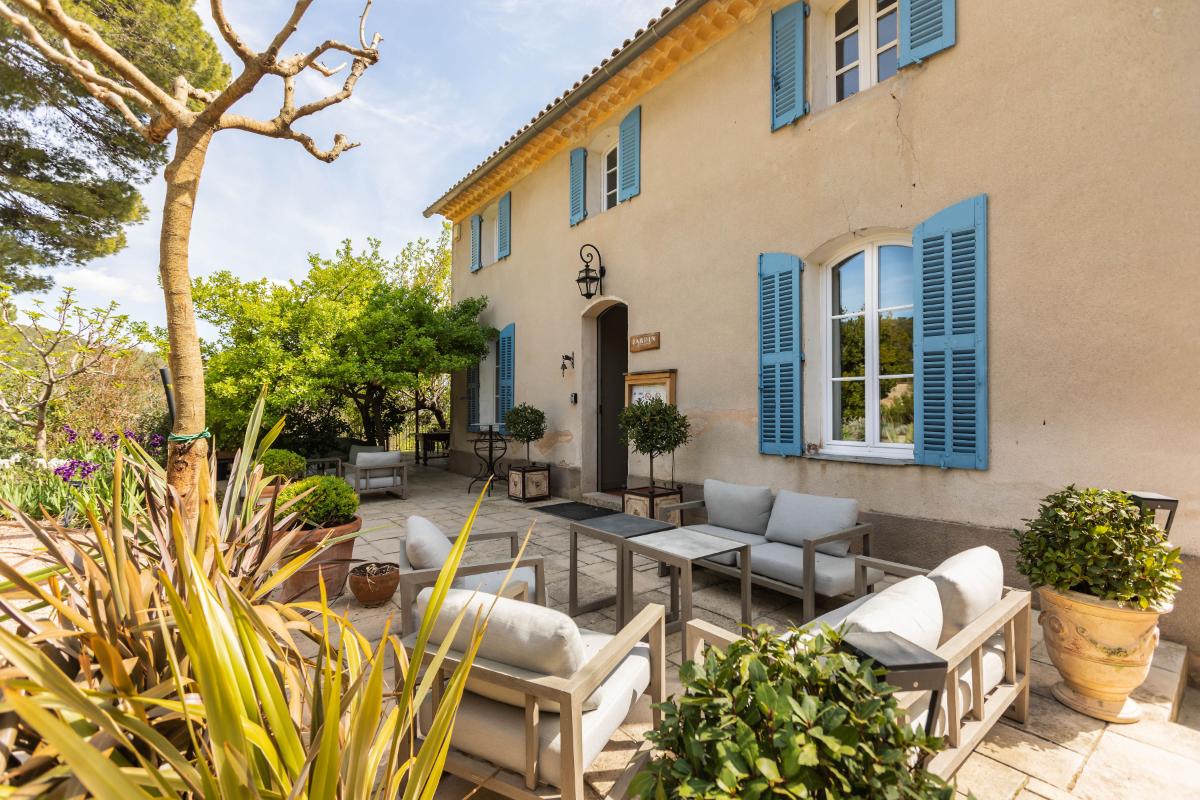 Le Restaurant terrace at Lou Calen with Provençal yellow building blue shutters and comfortable seating under glass canopy