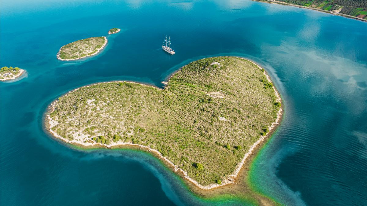 Aerial drone view of the Maxita yacht cruising near a green Croatian island with turquoise waters