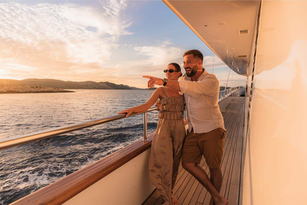 Couple posing on the yacht deck at sunset with a historic Croatian coastal town in the background
