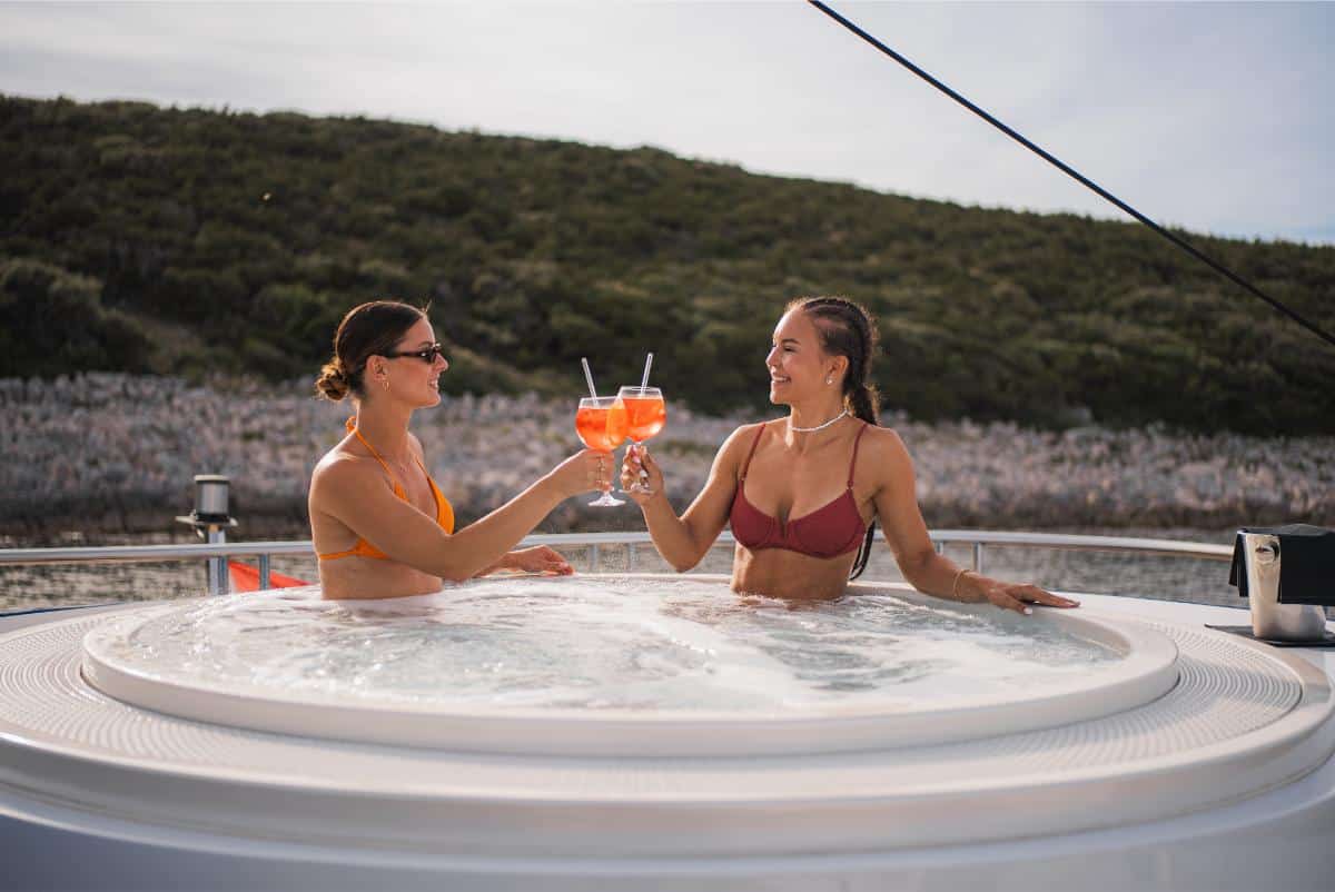 Couple toasting cocktails in a jacuzzi on a luxury yacht sundeck with ocean view