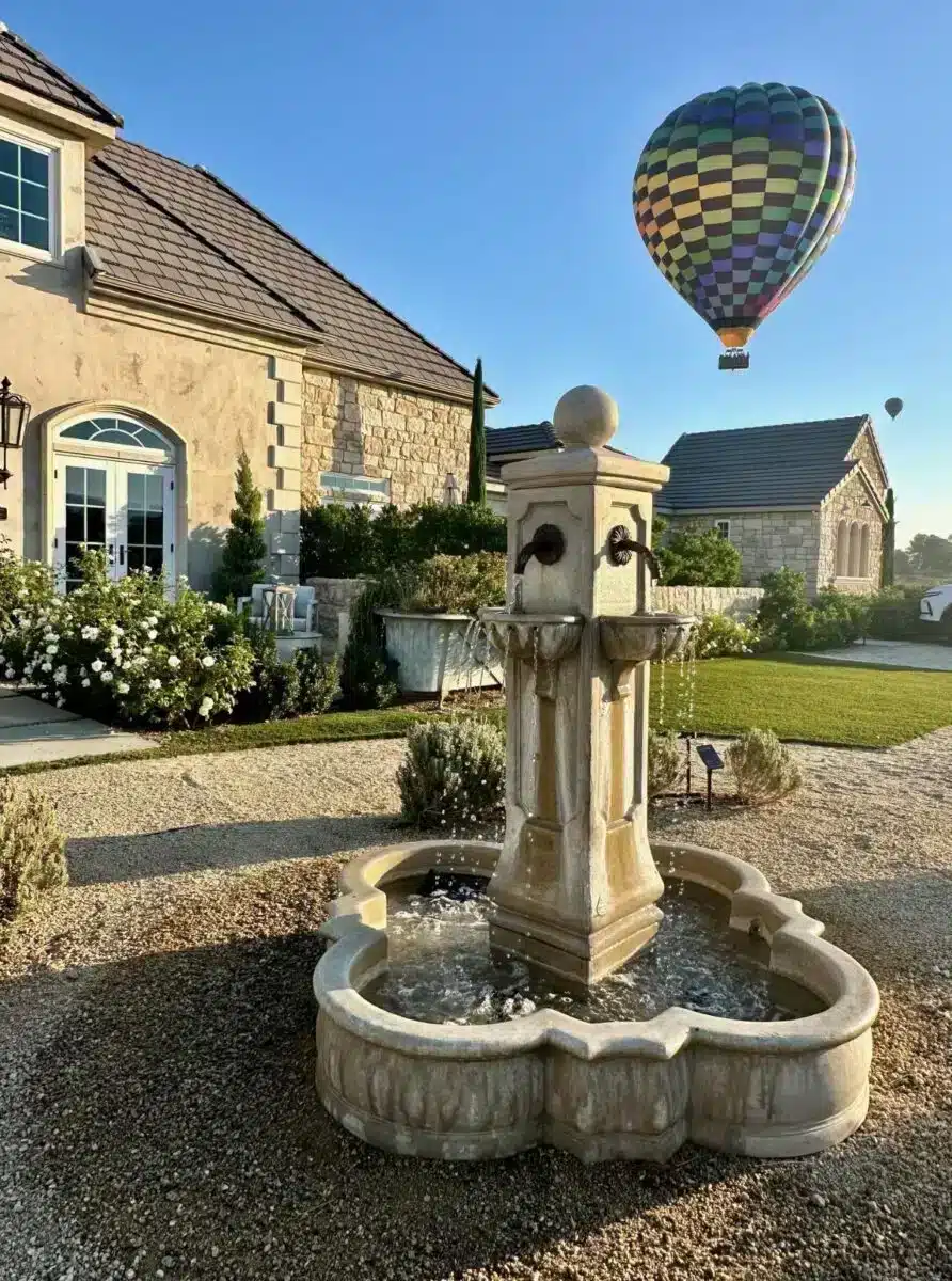 Stone courtyard fountain at Domaine Chardonnay wine estate in Temecula with a hot air balloon floating over the property in the morning sky