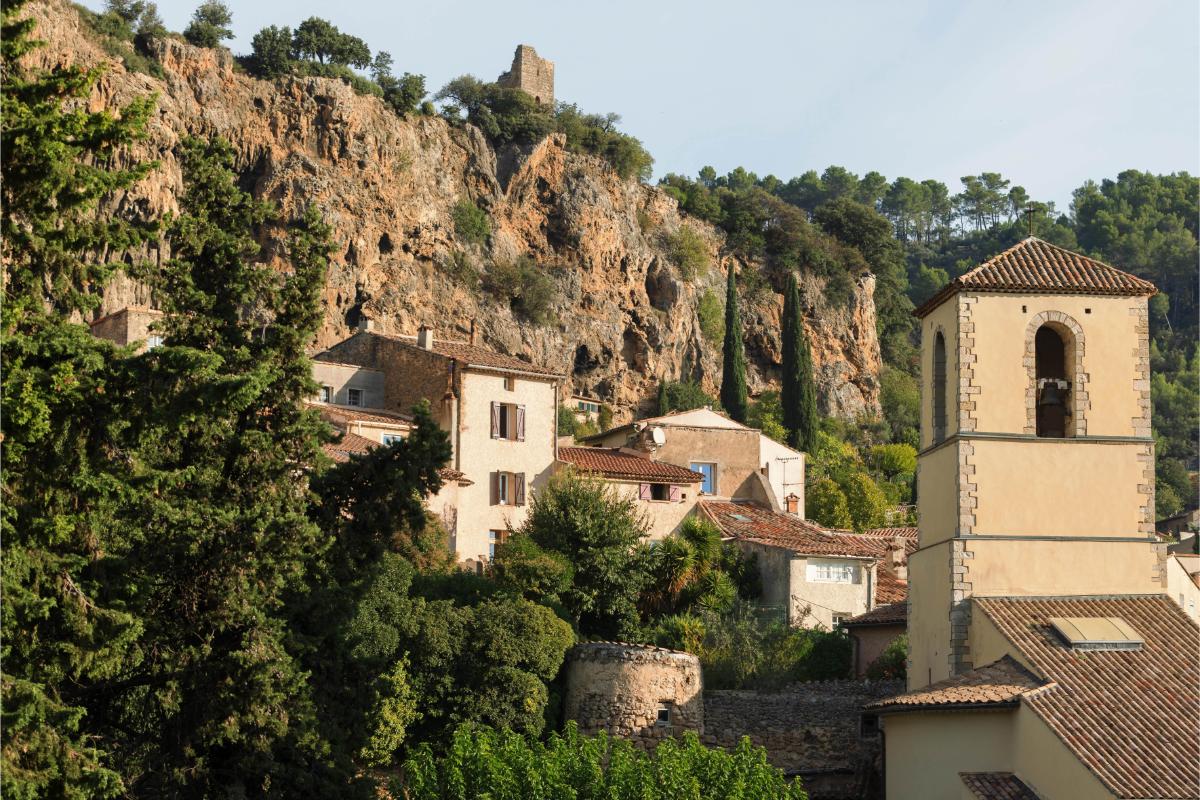 Village of Cotignac in Provence with stone buildings and bell tower beneath the dramatic red rock cliff face