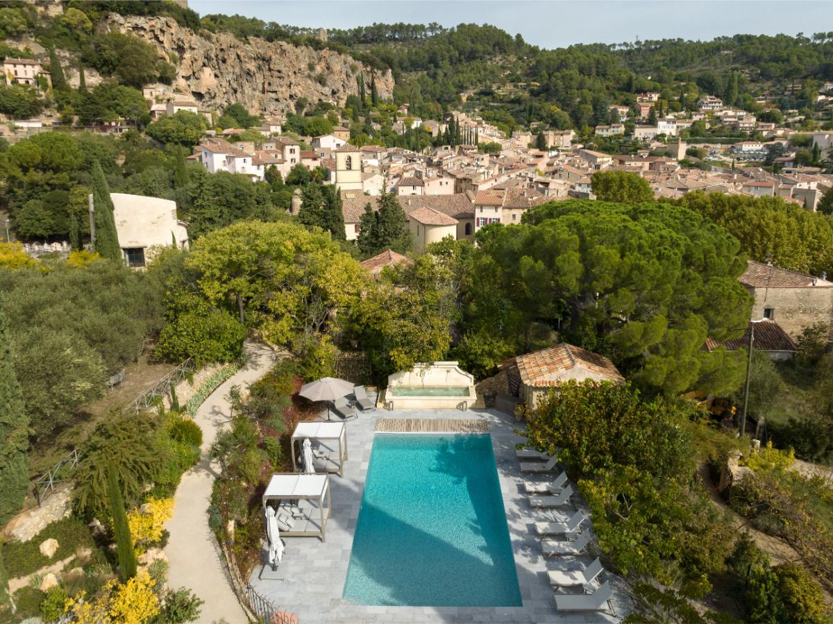 View of the Lou Calen domain with infinity pool cascading down the hillside among the village buildings of Cotignac