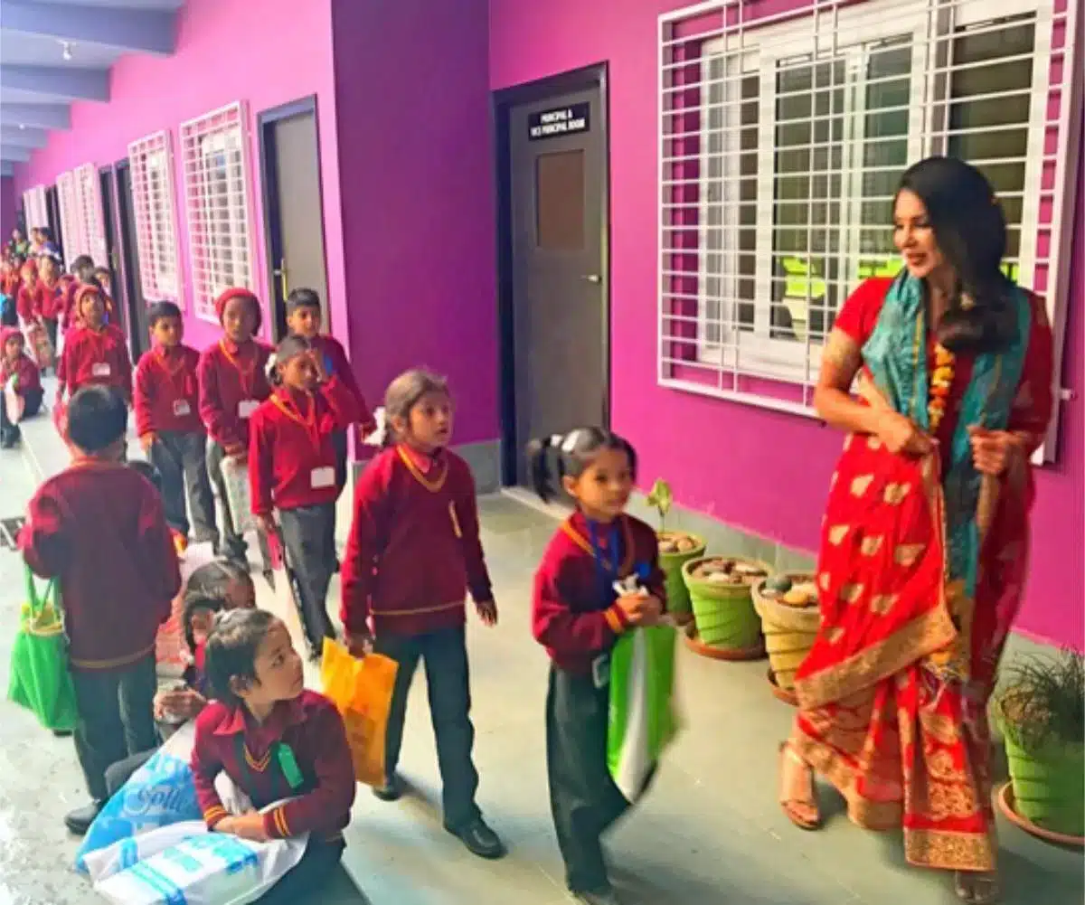 Sayé Yabandeh wearing a traditional red sari standing with schoolchildren in uniforms outside a school in India