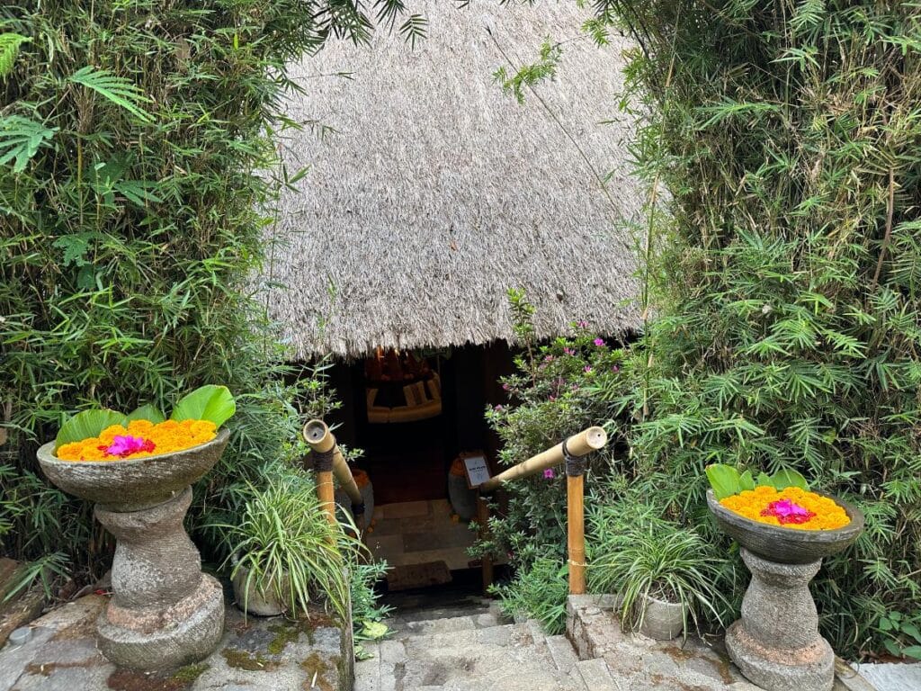 Traditional Balinese spa entrance at Munduk Moding Plantation with carved stone urns, marigold offerings and thatched pavilion