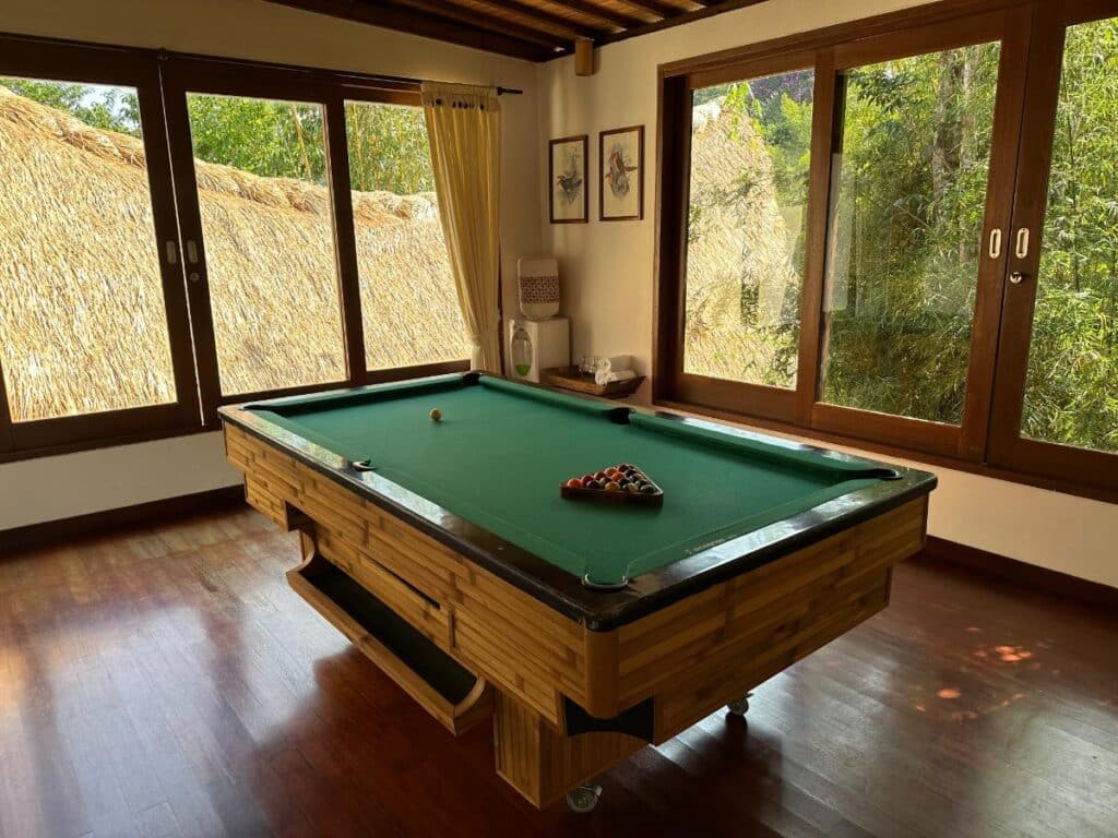Billiards room at Munduk Moding Plantation Bali with full-size pool table and highland garden views through glass windows