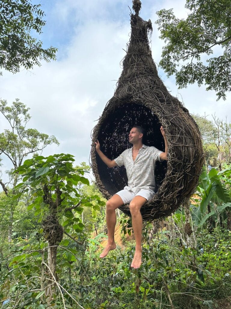 Guest sitting inside a large handwoven bird's nest art installation within the coffee plantation at Munduk Moding Plantation Bali
