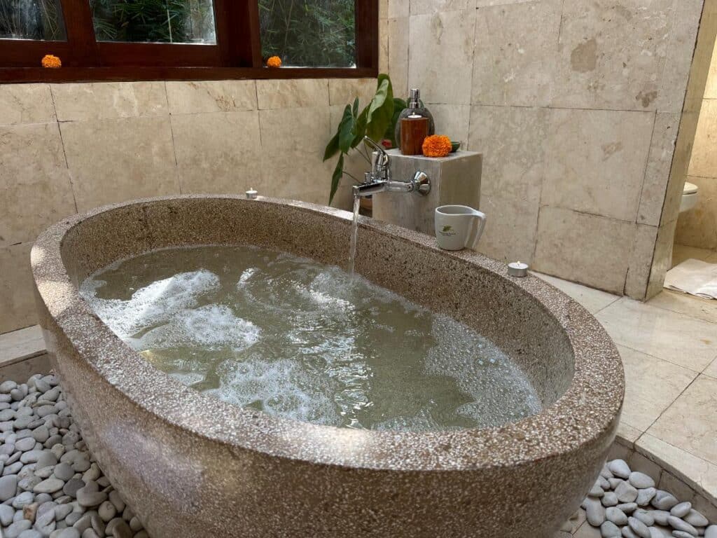 Guest enjoying a floating breakfast tray in the volcanic stone soaking bathtub at Munduk Moding Plantation Bali villa