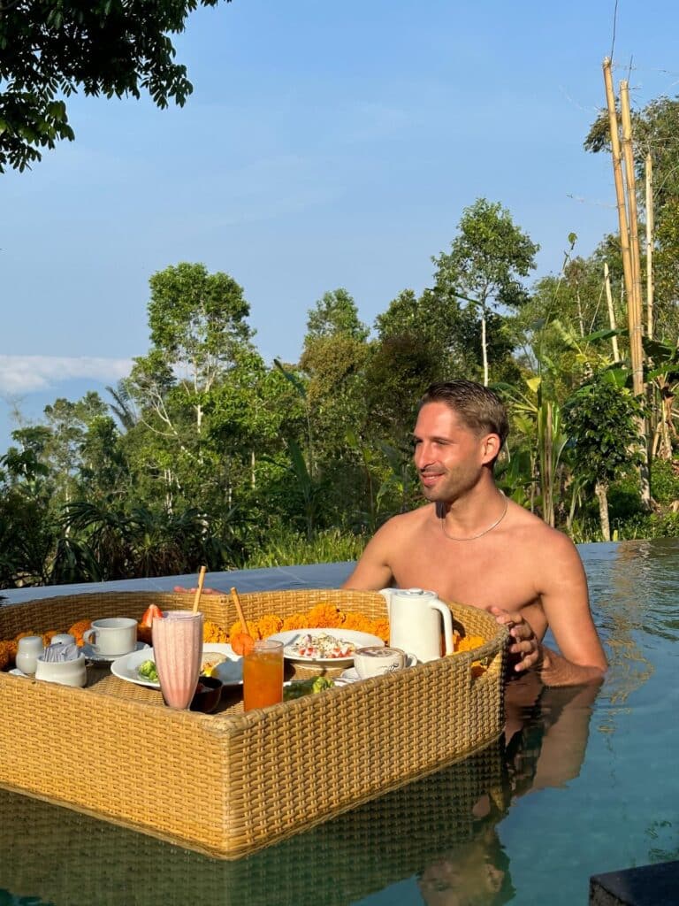 Man enjoying floating breakfast tray in private villa infinity pool at Munduk Moding Plantation Bali with Balinese highland jungle backdrop